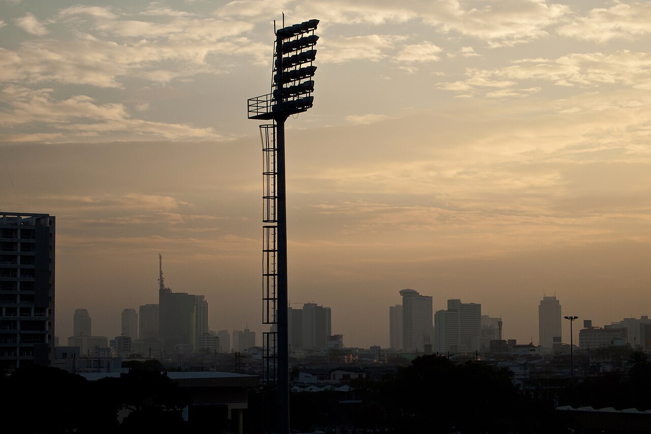 Bangkok skyline at sunset with a floodlight tower in the foreground, photographed in 2010.