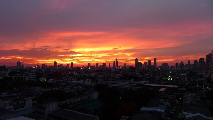 Bangkok skyline silhouetted beneath a vivid orange sunset.